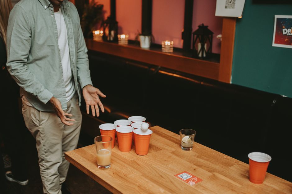 Casual beer pong game at a bar with a man standing beside a table with cups and ball.